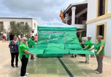 La AECC celebra la tradicional cuestación en la plaza de la Constitución de Formentera Despliegue bandera AECC en la plaza de la Constitución